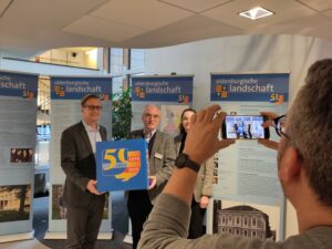 Eröffnung der Wanderausstellung zum Landschaftsjubiläum auf ihrer Station im Landkreis Wesermarsch am 4.2.2026 im Kreishaus Brake. vlnr.: Landrat Stephan Siefken, st. Geschäftsführer Oldenburgische Landschaft Dr. Jörgen Welp, Projektkoordinatorin Merle Bülter. Fotos SCS/Oldenburgische Landschaft